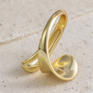 Détail macro d'une bague dorée ajustable en forme de vague au fini poli