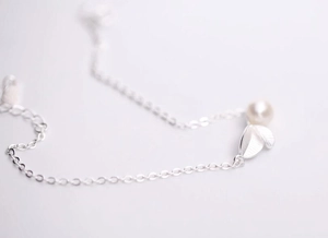 Vue macro d'un collier en argent S925 avec une perle blanche et des feuilles détaillées