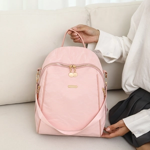 Detailed close-up of pink Oxford fabric backpack with gold zippers on a white sofa