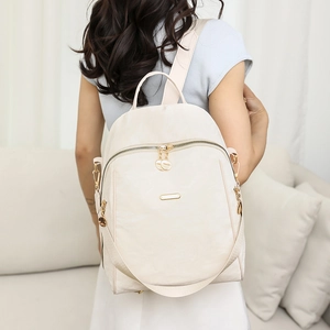Rear view of model wearing a cream oxford fabric backpack with gold zippers in cozy room