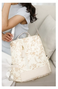 Détail d'un sac à dos beige à imprimé floral montrant la poche latérale et le pompon