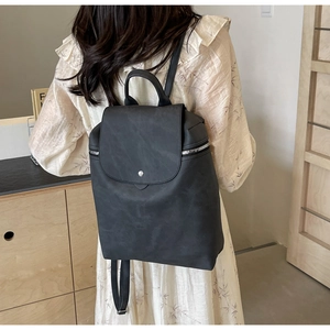 Detail view of a matte black PU leather backpack with flap closure on a model