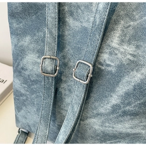 Detail of adjustable silver square buckles and washed denim fabric on the blue backpack