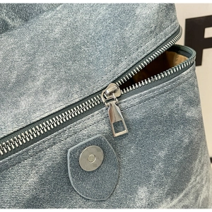 Detail of silver zipper and magnetic buckle on light blue denim texture backpack