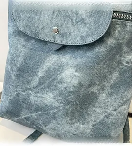 Detail of gray-blue backpack with denim texture, featuring a silver snap and metal zipper