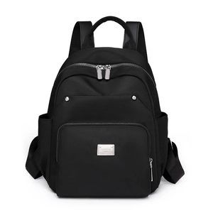 Detailed shot of black nylon backpack featuring front zip pocket and silver metal brand plate