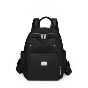Close-up of black nylon backpack featuring a silver metal logo plate and zip front pocket
