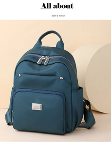 Detail of teal nylon backpack showing smooth texture, dual zippers, and metal brand plaque