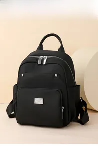 Close-up of black nylon mini backpack with silver double zippers and metal logo plate