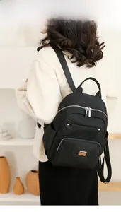 Model wearing a minimalist black nylon backpack with multiple zipper pockets for daily use