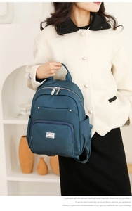 Detail of dark teal nylon backpack featuring multiple zip compartments and metal logo