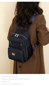 Minimalist black nylon backpack with silver zippers shown on a model in brown coat