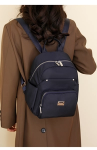 Detail of navy blue nylon backpack with silver zippers worn over a brown wool coat
