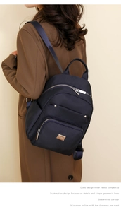 Detail of dark blue nylon backpack on model with focus on metallic zipper and brand plaque