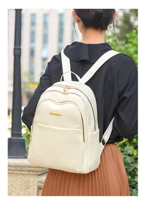Close-up of creamy white faux leather backpack with crocodile texture on a model outdoors
