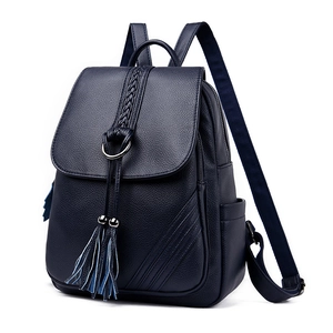 Detail of navy blue leather backpack with woven strap, metal ring and tassel accents