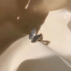Macro shot of 925 sterling silver butterfly ring with vintage textures on satin fabric