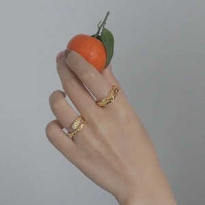 Stackable gold braided wide band and crystal open ring set on hand with an orange