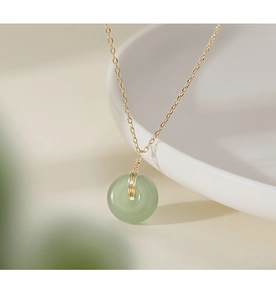 Macro shot of a pale green jade pendant on a gold chain over white ceramic background