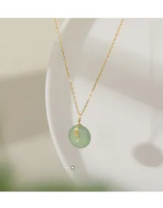 Detail of a jade peace buckle pendant with a fine gold-plated silver chain on white porcelain
