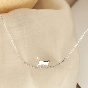 Détail du collier chat argenté montrant un chat marchant sur une barre courbe sur lin