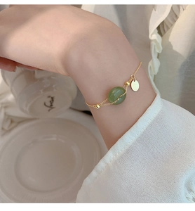 Detail of round green Hetian jade bracelet with 18K gold plating on a woman's wrist