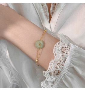 Detail of jade donut bracelet with gold-plated chains on a lace fabric sleeve