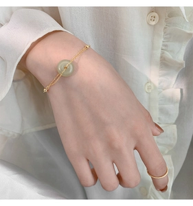 Close-up of a gold jade bracelet and twist ring on a model wearing a white shirt
