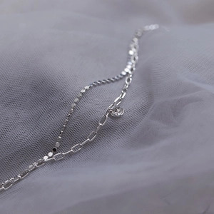 Detail of double-layer S925 sterling silver bracelet with round tag on white tulle