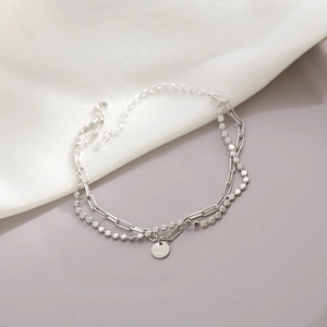 Macro shot of silver layered chain bracelet with lucky coin pendant and refined textures