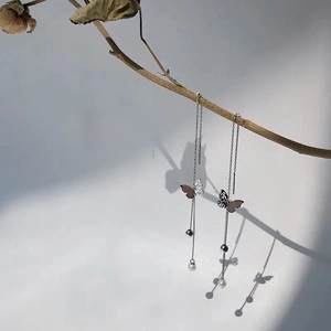 Detail of silver butterfly tassel earrings with long chains and white pearls on a branch