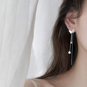 Close-up of butterfly pearl drop earrings with elegant tassels on a model's ear