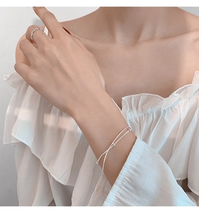Close-up of minimalist double-layer silver snake chain bracelet and wavy ring on model