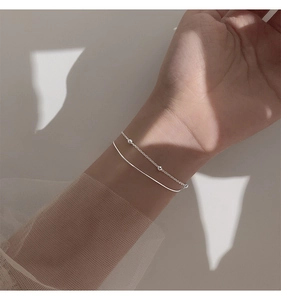 Detail of silver double-layered snake chain bracelet worn on wrist with aesthetic lighting