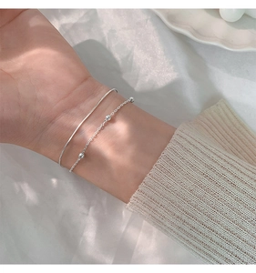 Close-up of a double-layered silver bracelet set featuring a sleek cuff and beaded chain