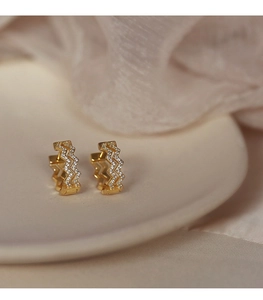 Close-up of gold wave-shaped hoop earrings with micro-set zircons on ceramic plate