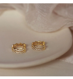 Detailed close-up of gold wavy hoop earrings with zircon pavé on soft silk background