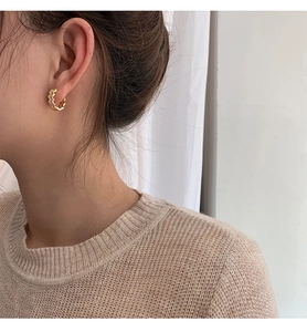 Detail of gold wavy earrings with zircon inlays worn by a model in soft lighting