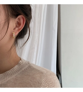 Detail of gold-plated wave-shaped hoop earrings with micro-inlaid cubic zirconia on ear