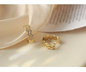 Detail of gold wave hoop earrings with micro zircons on champagne silk background
