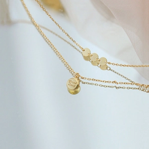 Macro shot of gold 'Good Luck' engraved pendant on a delicate layered silver necklace
