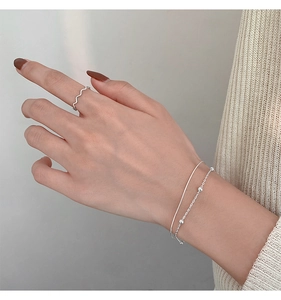 Detail of layered silver beaded bracelets and minimalist wavy ring on model wrist