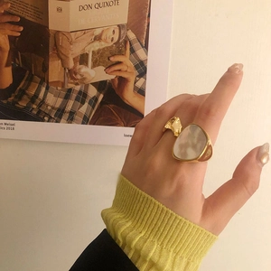 Gros plan d'une bague en nacre blanche irrégulière dorée au doigt d'une femme
