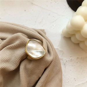 Bague en argent s925 doré avec nacre blanche triangulaire sur un tissu tricoté beige