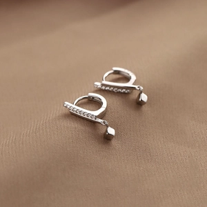 Macro detail of S925 silver cube drop earrings with micro-set zircon bar on brown fabric