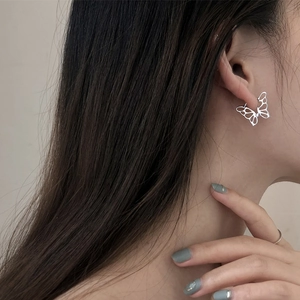 Close-up of a silver hollow butterfly earring worn on ear with soft lighting