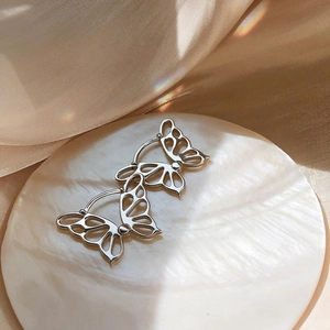 Detailed macro shot of silver butterfly earrings with hollow wings on a silk fabric background