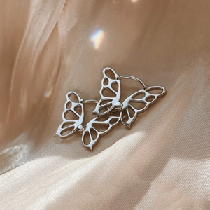 Hollow butterfly hoop earrings in silver finish on champagne silk background