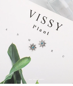 Macro shot of silver sunflower stud earrings with blue zircon on a minimalist card