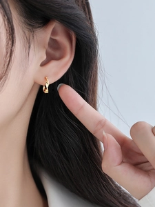 Close-up of golden Mobius twist hoop earrings worn by a model for a minimalist aesthetic